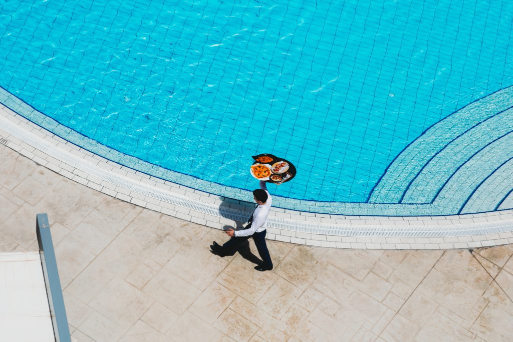 man carrying tray of food by pool