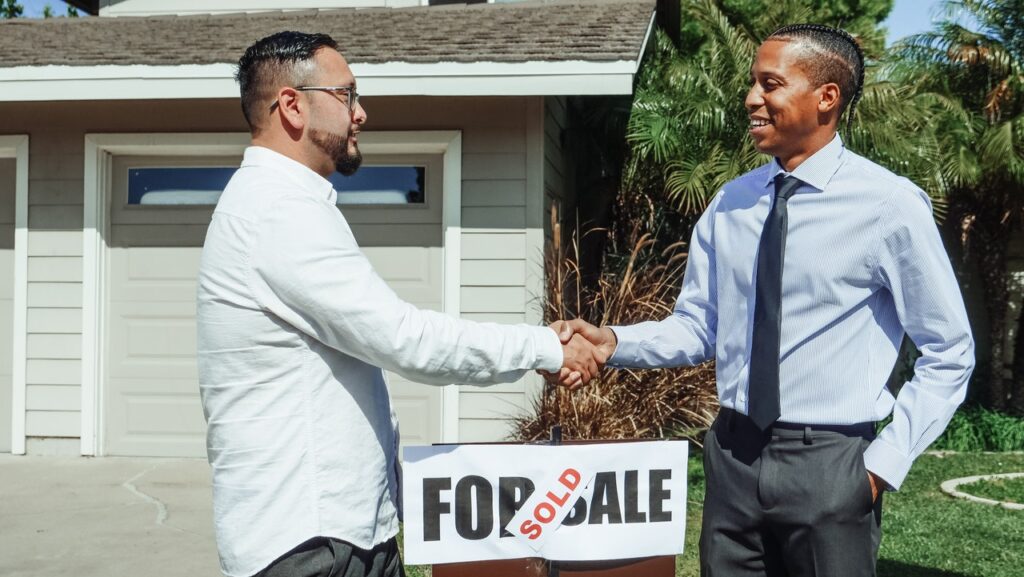 two man shaking hands in front of a home