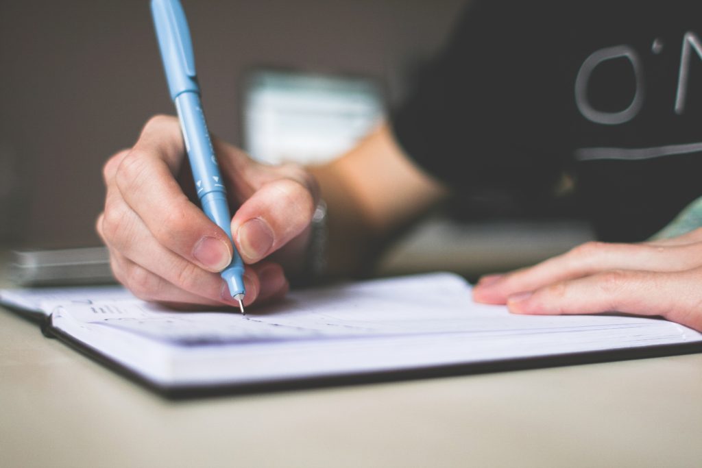 person-holding-blue-ballpoint-pen-writing-in-notebook