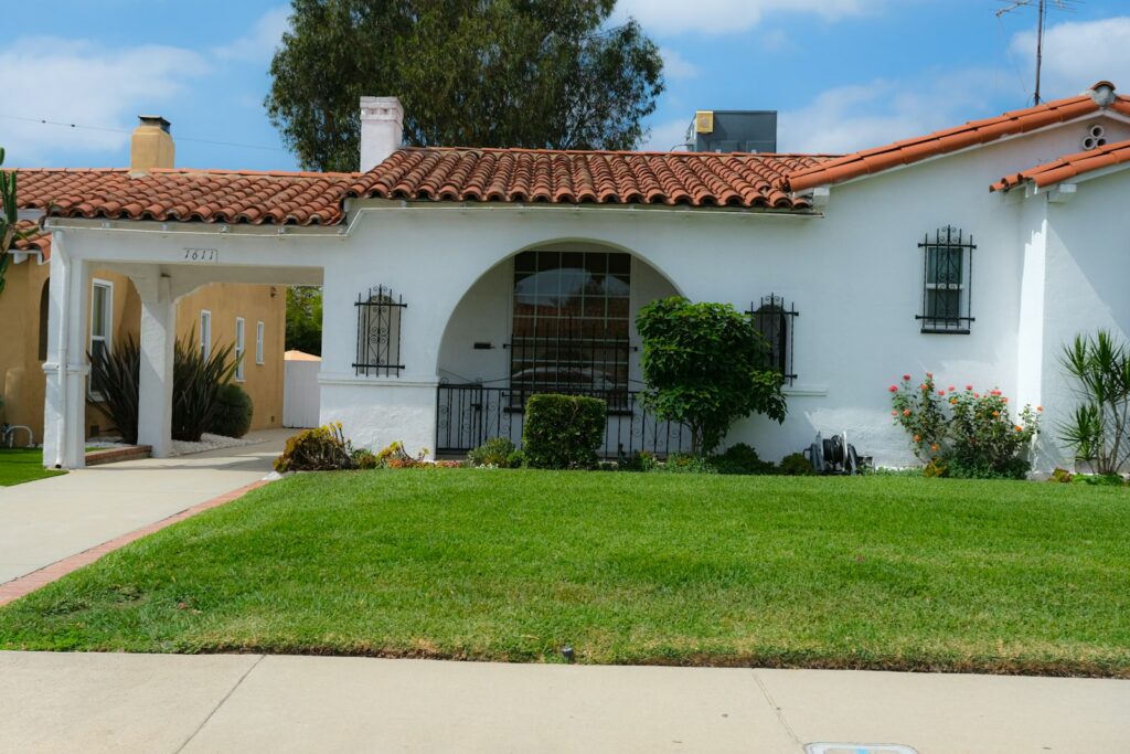 White stucco single family home with a red tile roof and front lawn in a Southern California suburb