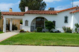 White stucco single family home with a red tile roof and front lawn in a Southern California suburb