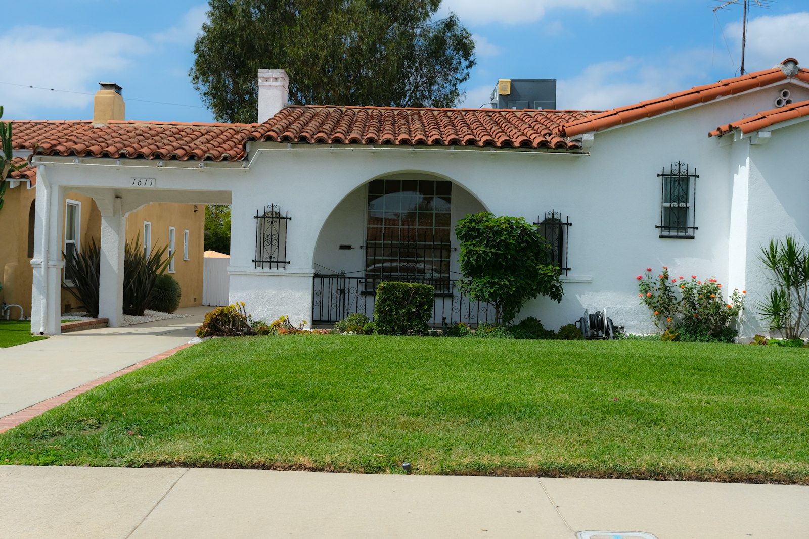 White stucco single family home with a red tile roof and front lawn in a Southern California suburb